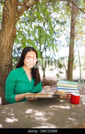 Jolie jeune femme lisant des livres sur le terrain sous un saule, avec une tasse de café. Journée mondiale du livre Banque D'Images