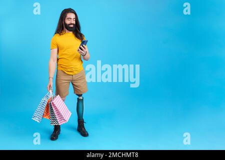 Homme avec une jambe prothétique utilisant les sacs de shopping de loing mobile Banque D'Images