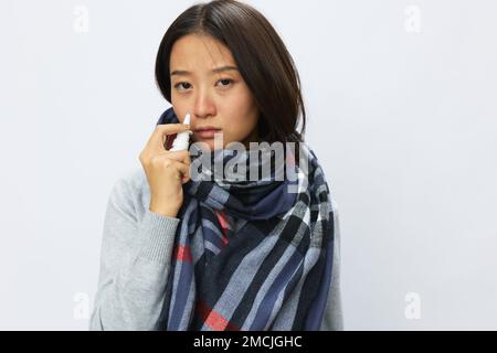 Femme asiatique grippe rhume avec nez bouché contient le spray nasal et vaporise le spray nasal pour les allergies et le virus Covid 19 avec mal de gorge sur fond blanc Banque D'Images