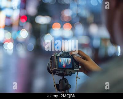 Dans la rue au Japon, un photographe photographie les lumières de nuit sous la pluie de Tokyo et de Shinjuku avec son appareil photo sans miroir sur un trépied. Banque D'Images