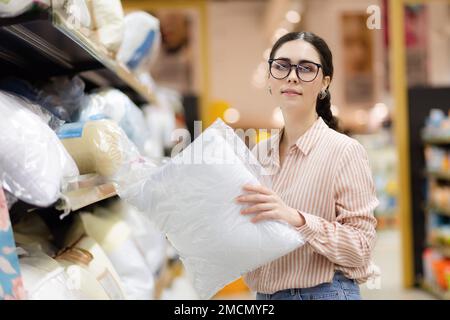 Portrait de caucasienne jolie femme portant des lunettes tient l'oreiller. Textiles domestiques au supermarché. Concept commercial. Banque D'Images