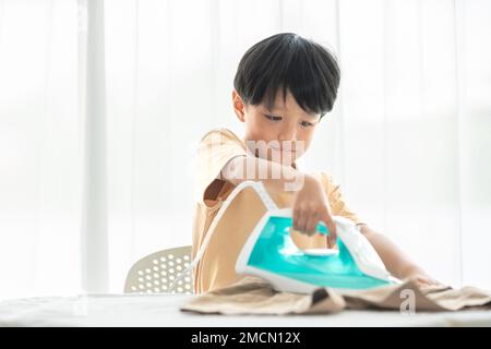 jeune garçon heureux fer son uniforme d'école avec fer sur planche à repasser à la maison pendant le week-end pour le nettoyage de la maison activité familiale Banque D'Images