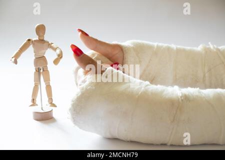 deux mains femelles avec poignets cassés après être tombée d'une bicyclette dans un casting sur un fond isolé avec un petit mannequin en bois d'un homme, les mains dans un ca Banque D'Images