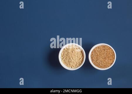 Vue de dessus d'un ensemble de graines de lin écrasées sur deux bols ronds différents de nourriture en céramique côte à côte sur un fond bleu studio avec espace de copie. En bonne santé Banque D'Images