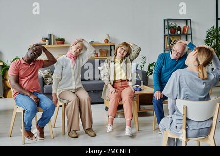 Groupe de personnes âgées assises sur des chaises et faisant des exercices physiques avec un instructeur Banque D'Images