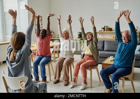 Groupe de personnes âgées assises sur des chaises et s'exerçant pendant l'entraînement sportif avec un instructeur Banque D'Images