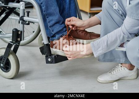 Gros plan d'une jeune femme aidant un homme handicapé à attacher des lacets pendant qu'il est assis en fauteuil roulant Banque D'Images