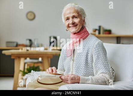 Portrait d'une femme âgée souriant à la caméra tout en étant assise sur un fauteuil et brodant Banque D'Images