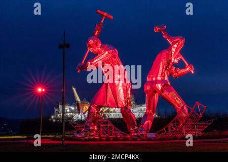 Greenock, Royaume-Uni. 21 janvier 2023 en photo : la sculpture des constructeurs de navires de Port Glasgow de John McKenna est illuminée devant le Glen Sannox Ferry en cours de construction au chantier naval Ferguson. Crédit : Rich Dyson/Alay Live News Banque D'Images