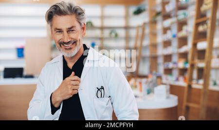 Médecin debout dans une pharmacie sous une blouse de laboratoire. Un professionnel de la santé mûr souriant à la caméra. Homme senior travaillant dans un chimiste. Banque D'Images