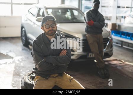 Mécanique automobile dans un atelier de réparation automobile, l'un d'entre eux assis sur une pile de roues de voiture. Photo de haute qualité Banque D'Images