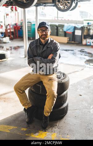 Un homme assis sur une pile de roues de voiture dans un atelier de réparation de voiture moderne et bien équipé. Photo de haute qualité Banque D'Images