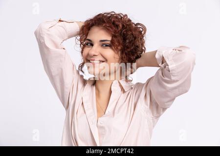 Une fille souriante corrige ses cheveux bouclés avec deux mains. Européen. Banque D'Images