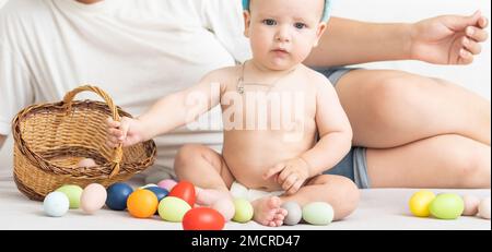 Maman et bébé avec des oreilles de lapin, avec des œufs de Pâques dans leurs mains, assis sur le canapé, parents et enfants jouent à l'intérieur. La famille fête Pâques Banque D'Images