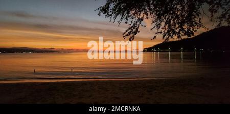 Une vue panoramique sur le coucher de soleil orange et l'éclairage se reflétant sur une plage avec des montagnes Banque D'Images