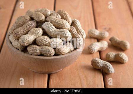 Bol plein de cacahuètes décortiquées sur fond de bois, vue de dessus Banque D'Images