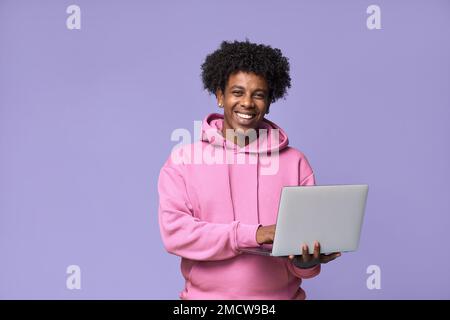 Adolescent africain heureux tenant avec un ordinateur portable isolé sur fond violet. Banque D'Images