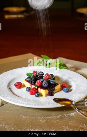 Une tranche de cheesecake aux framboises fraîches et aux mûres et une couche de sucre glace sur une assiette blanche Banque D'Images