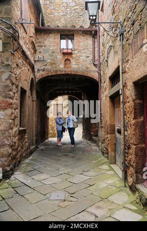 Scène de rue médiévale, arquée en pierre Cour pavée en pierre avec deux piétons, village de montagne Roccatederighi, Toscane Italie, Banque D'Images