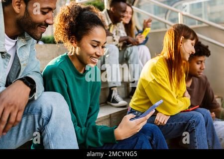 Jeune groupe de personnes diverses utilisant le téléphone mobile à l'extérieur Banque D'Images