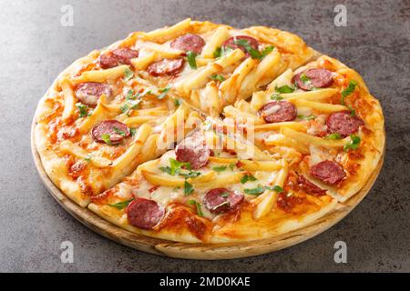 Savoureuse pizza Americana avec frites, wurstel, fromage, sauce tomate et herbes gros plan sur une planche de bois sur la table. Horizontale Banque D'Images