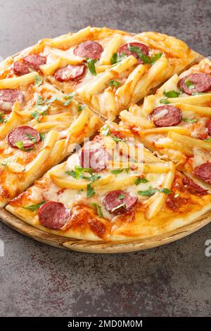 Pizza chaude fraîchement cuite avec frites, saucisses, fromage, sauce tomate en gros plan sur une planche de bois sur la table. Verticale Banque D'Images