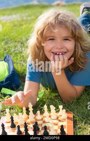 Un petit gamin joue aux échecs dans le parc. Enfant garçon jouant à un jeu de société à l'extérieur. Réflexion enfant brainstorming et idée dans le jeu d'échecs Banque D'Images