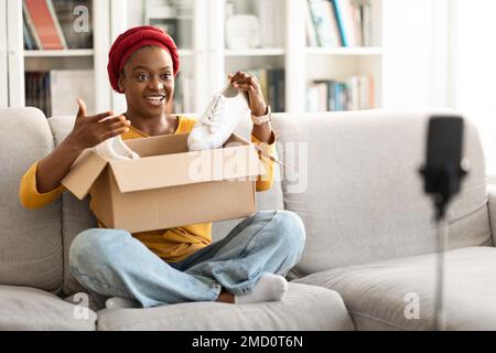 Influenceur des médias sociaux jeune femme noire examinant le produit nouvelles chaussures Banque D'Images