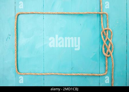 Cadre rectangulaire en corde de jute, avec un nœud sur des planches peintes en bleu, toile de fond bleu marine Banque D'Images
