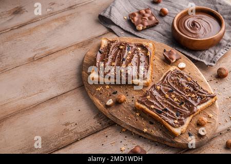 Planche de pain avec pâte de chocolat et bonbons de fête saupoudrer et noisettes sur fond de bois. Nourriture populaire de dessicer. Vue de dessus. Banque D'Images