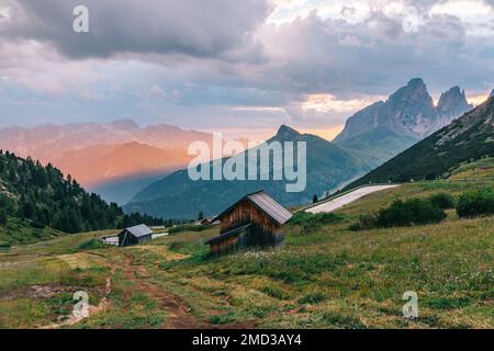 Maisons traditionnelles en bois dans les Alpes italiennes dans un paysage cinématographique à la lumière dorée, une route de montagne et d'impressionnantes montagnes. Dolomites, Italie. Banque D'Images