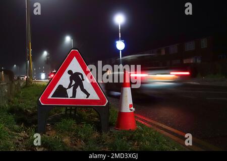 Un panneau triangulaire de signalisation routière et un cône de circulation sur le côté d'une route la nuit aux automobilistes portés de travaux routiers devant, Banque D'Images