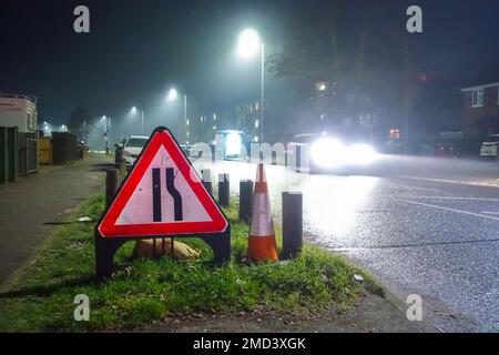 Un panneau triangulaire de signalisation routière et un cône de circulation sur le côté d'une route la nuit pour les automobilistes portés d'une route rétrécie devant vous, Banque D'Images