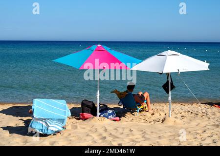 Homme relaxant sous des parasols de plage sur une plage, région de la Sardaigne, Italie Banque D'Images