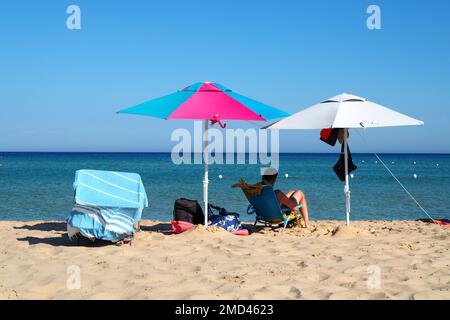 Homme relaxant sous des parasols de plage sur une plage, région de la Sardaigne, Italie Banque D'Images