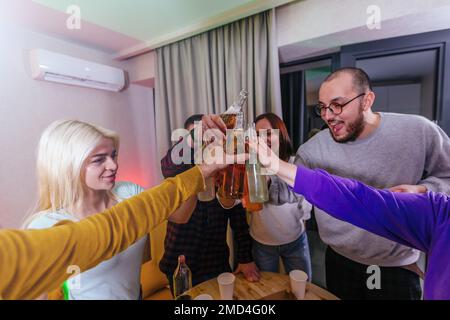 Fête à domicile. Les gens heureux sont de clinking bouteilles de bière à un toast. Banque D'Images