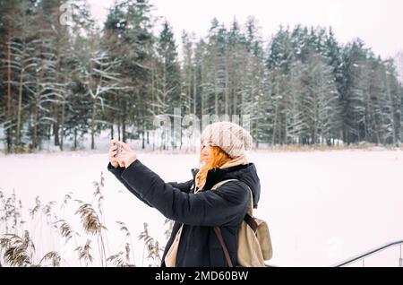 femme en hiver avec le téléphone prend des photos de la nature dans le parc par temps froid Banque D'Images