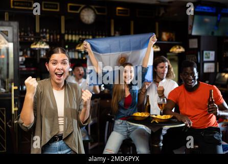 Bonne fille qui applaudisse émotionnellement à l'équipe préférée de l'Argentine dans le bar des sports Banque D'Images