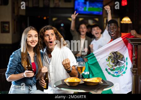 Les amateurs de sport multiracial agitant le drapeau du Mexique tout en buvant de la bière dans le bar sportif Banque D'Images