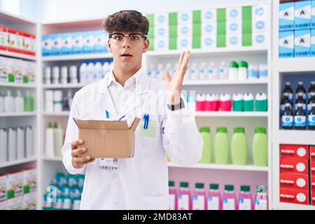 Adolescent hispanique travaillant à la pharmacie drugstores holding box avec des pilules célébrant la victoire avec le sourire heureux et l'expression du gagnant avec les mains levées Banque D'Images