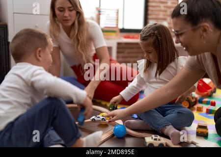 Enseignants avec un garçon et une fille jouant avec des voitures jouet assis sur le sol à la maternelle Banque D'Images