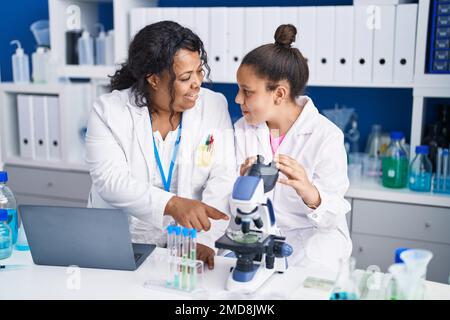 Mère et fille scientifiques utilisant un microscope et un ordinateur portable travaillant en laboratoire Banque D'Images