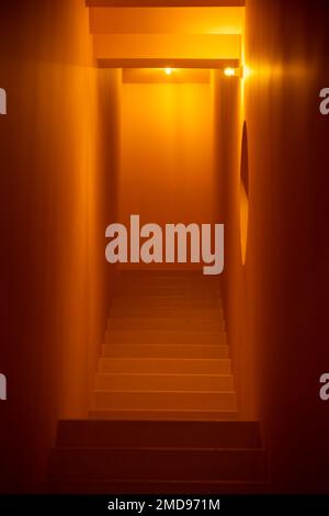 Vue verticale de bas en haut de l'escalier en pierre intérieur d'un bâtiment dans un petit couloir étroit, éclairé par un éclairage chaleureux, à faible profondeur Banque D'Images