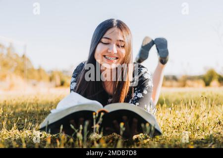 Gros plan d'une jeune femme couché en lisant la bible sur l'herbe avec un arrière-plan flou Banque D'Images