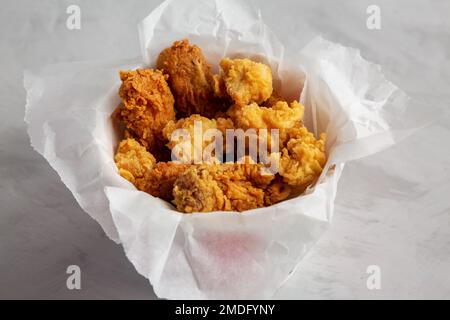 Pop-corn au poulet, ailes, filets dans une boîte en papier sur fond gris, vue latérale. Gros plan. Banque D'Images