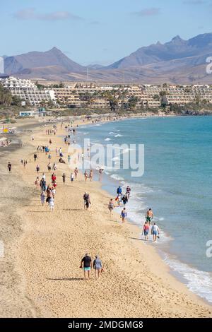 Touristes se promenant sur la plage au sud de Costa Calma. Montagnes et installations touristiques en arrière-plan. Fuerteventura, îles Canaries. Banque D'Images