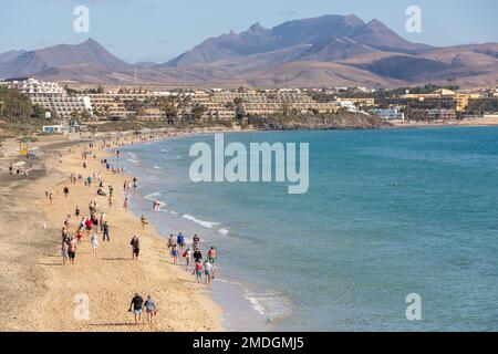 Touristes se promenant sur la plage au sud de Costa Calma. Montagnes et installations touristiques en arrière-plan. Fuerteventura, îles Canaries. Banque D'Images