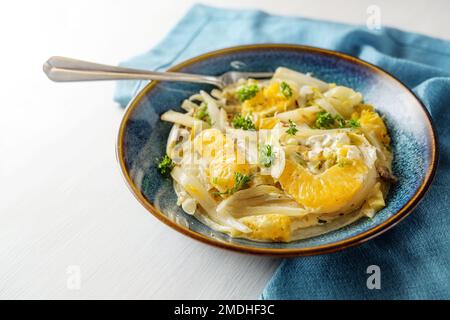 Plat de chicorée et d'orange avec oignons de printemps sur une assiette bleue et serviette sur une table en bois blanc, repas végétarien sain pour un régime bas de carb, copie sp Banque D'Images