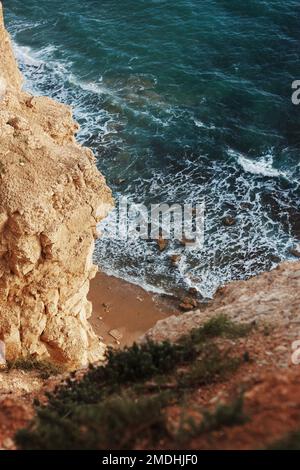 Une vue verticale depuis le bord de mer abrupte falaises de vagues de mer s'écrasant dans la plage de sable Banque D'Images