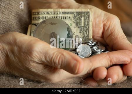 Les dollars américains et les centimes ukrainiens et un globe de verre de la planète se trouvent entre les mains d'une vieille femme, de la finance et du peuple Banque D'Images